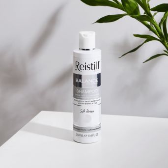 Reistill Balance SOS Program Hair Loss Prevention Shampoo 250 ml on white table with green plant, stimulating care for weak thinning hair