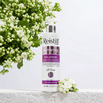 Reistill Nutritive Deep Balsamo Conditioner for curly hair placed beside white blossoms on a light textured surface